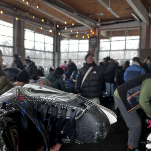 A hockey skate being held up in front of a packed room of people with twinkly lights and lots of windows.